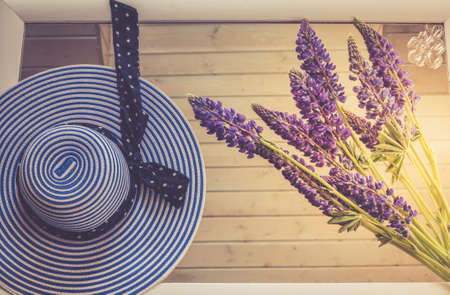 Female hat, in stripes, top view. Conceptual image. Female hat and lupine flowers, on a mirror background. Blue colour.の写真素材