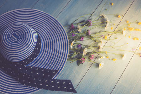 Female hat, striped, bouquet of wildflowers, top view. On a wooden background. Blue color. Conceptual image.Horizontal photoの写真素材