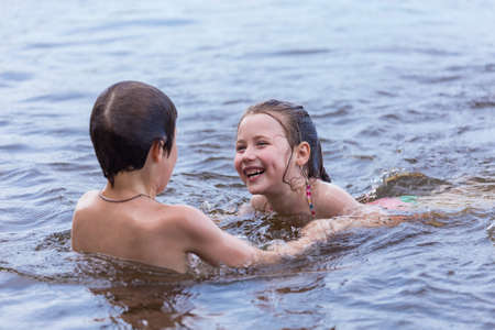 Little boy teaches his little sister to swim in a lakeの写真素材