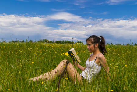 Young woman reading book on a meadowの写真素材