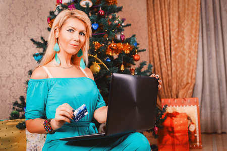 Pretty woman with laptop and credit card buying presents near Christmas treeの写真素材