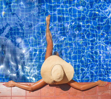 Young slim woman in hat sitting in swimming pool outdoorsの写真素材