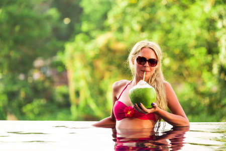 Young pretty blonde woman in swimming pool with coconut cocktail drinkの写真素材