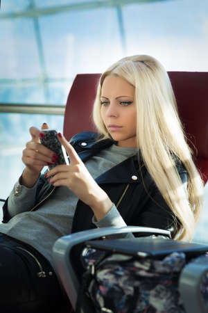 Young pretty blonde woman with mobile phone sitting in arportの写真素材