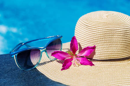 Blue sunglasses and straw hat with orchid flower near swimming pool - holiday conceptの写真素材