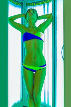 Slim young woman standing in solarium getting perfect sun tanの写真素材