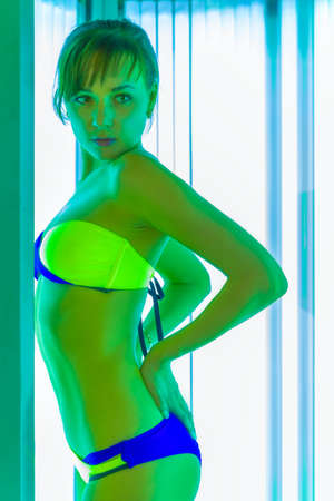 Slim young woman standing in solarium getting perfect sun tanの写真素材