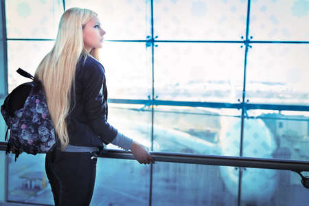 Young pretty blonde woman looking into window in airportの写真素材