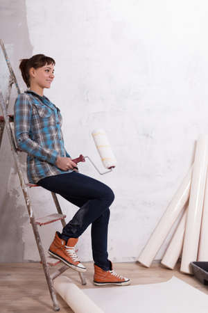 Pretty woman with roller paste wallpaper to repair houseの写真素材