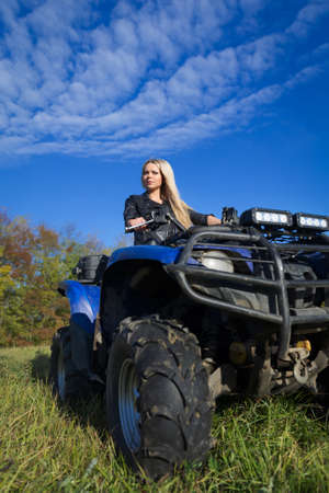 Elegant blonde slim woman riding ATV on a fieldの写真素材