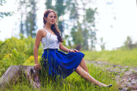 Young pretty woman poses showing dress summer outdoors in sunset lightの写真素材