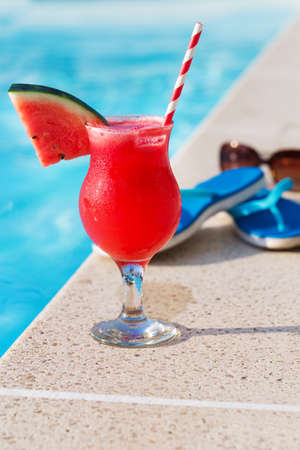 Water melon red fresh juice smoothie drink cocktail slippers and sunglasses near swimming poolの写真素材