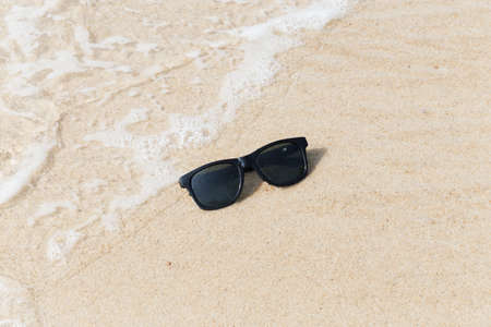 Black sunglasses on the beach in waterの写真素材