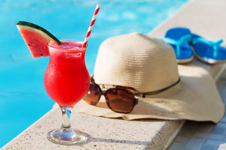 Water melon red fresh juice smoothie drink cocktail slippers, straw hat and sunglasses near swimming poolの写真素材
