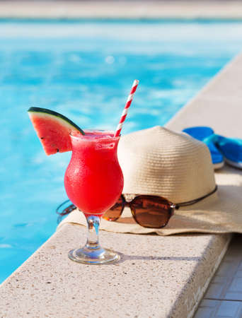 Water melon red fresh juice smoothie drink cocktail slippers, straw hat and sunglasses near swimming poolの写真素材