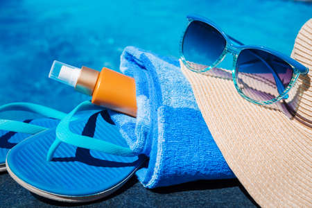 Blue slippers, sunsscreen cream, straw hat and sun glasses near swimming pool - holiday conceptの写真素材