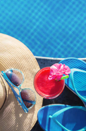 Water melon red fresh juice smoothie drink cocktail slippers, straw hat and sunglasses near swimming poolの写真素材