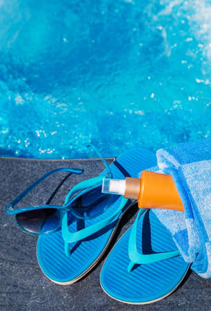 Blue slippers, sunsscreen cream and sun glasses near swimming pool - holiday conceptの写真素材