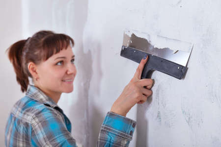 house improvement by woman worker puts finishing layer of stucco on the wall using a plastering trowelの写真素材