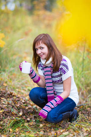 Pretty woman with tea cup in an autumn parkの写真素材