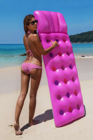 Young slim brunette woman in sunglasses gets suntan with an air mattress on the tropic beachの写真素材