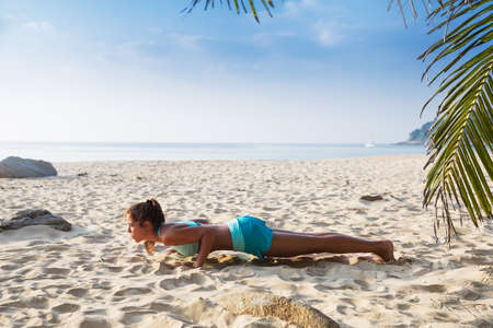 Young pretty slim brunette woman practise yoga Four-limbed staff Chaturanga Dandasanapose on a tropical beachの写真素材