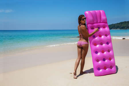 Young slim brunette woman in sunglasses gets suntan with an air mattress on the tropic beachの写真素材