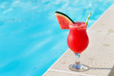 Glass of fresh watermelon smoothie juice drink on border of a swimming pool - holiday tropical conceptの写真素材