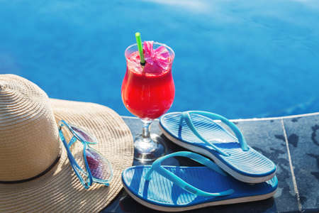 Watermelon fresh juice smoothie drink glass with flower, sunglasses, slippers and straw hat on border of a swimming pool - holiday tropical conceptの写真素材
