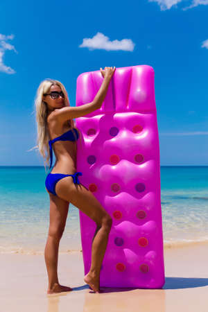 Young slim blonde woman in sunglasses gets suntan with an air mattress on the tropic beachの写真素材