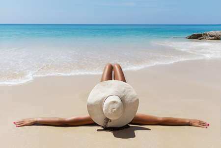 Young pretty slim brunette woman in hat and sunslasses sunbathe on the tropical beach in bikiniの写真素材
