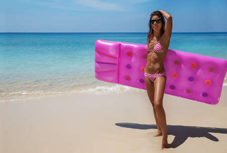 Young slim brunette woman in sunglasses sunbathe with an air mattress on the tropic beachの写真素材