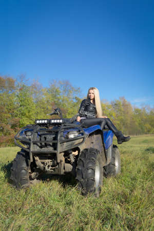Elegant blonde woman riding extreme quadrocycle ATV on a summer fieldの写真素材