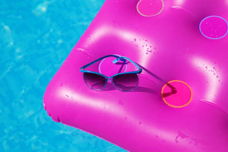 Sunglasses with pink mattress at the swimming pool - holiday tropical conceptの写真素材