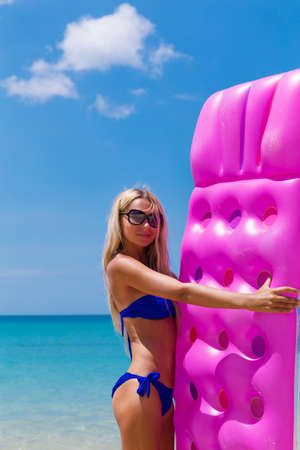 Young slim blonde woman in sunglasses gets suntan with an air mattress on the tropic beachの写真素材