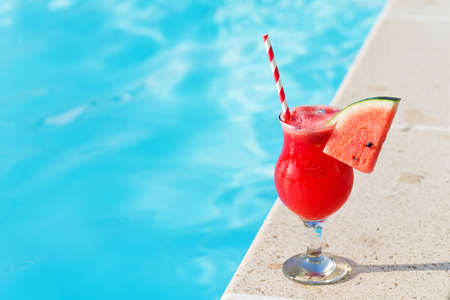 Glass of fresh watermelon smoothie juice drink on border of a swimming pool - holiday tropical conceptの写真素材