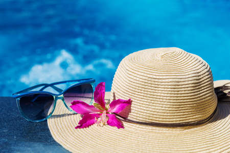 Sunglasses with flower and straw hat on border of a swimming pool - holiday tropical conceptの写真素材