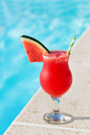 Glass of fresh watermelon smoothie juice drink on border of a swimming pool - holiday tropical conceptの写真素材