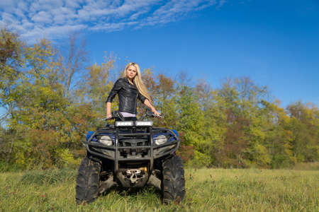 Elegant blonde woman riding extreme quadrocycle ATV on a summer fieldの写真素材