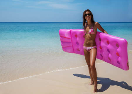 Young slim brunette woman in sunglasses sunbathe with an air mattress on the tropic beachの写真素材