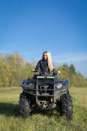 Elegant blonde woman riding extreme quadrocycle ATV on a summer fieldの写真素材
