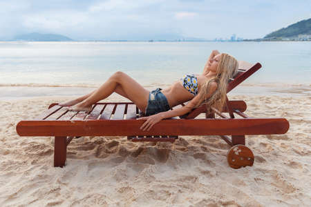 beautiful young slim blonde woman girl gets suntan on a sunbed near the seaの写真素材