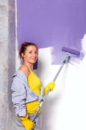young attractive woman paints white wall and purple paint rollerの写真素材