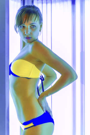 Slim young woman standing in solarium getting sun tanの写真素材