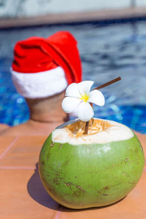 Coconut juice drink with man in Christmas Santa hat at the swimming pool - holiday tropical conceptの写真素材