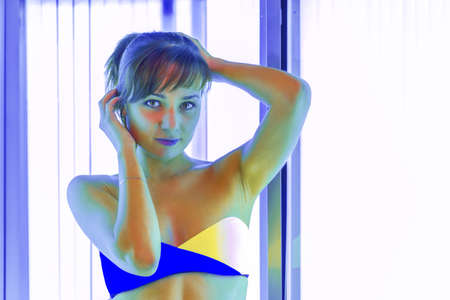 Slim young woman standing in solarium getting sun tanの写真素材