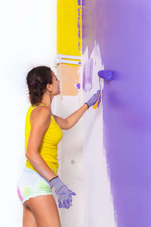 young attractive woman paints white wall and purple paint rollerの写真素材