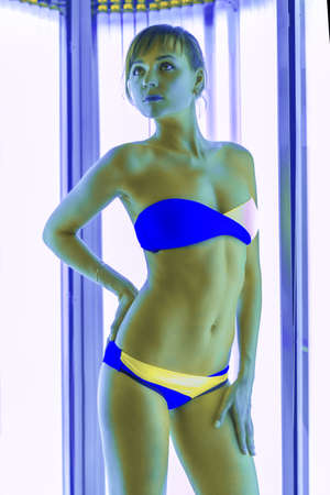 Slim young woman standing in solarium getting sun tanの写真素材