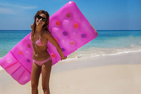 Young slim brunette woman in sunglasses sunbathe with an air mattress on the tropic beachの写真素材