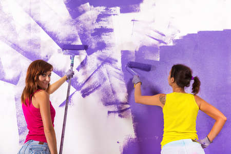 young beautiful women paints white wall and purple paint rollerの写真素材
